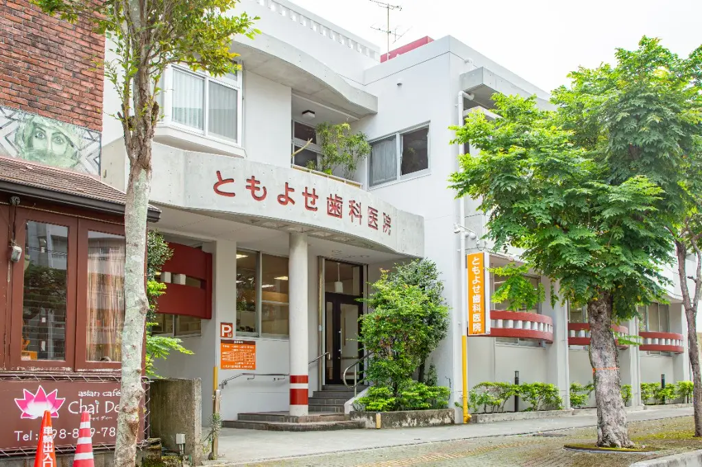 ともよせ歯科医院の外観。白い建物に赤字で医院名が表示されています。